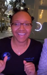 Headshot of Mrs. Sampson in a black v-neck NMSS t-shirt, wearing glasses, and smiling at the camera