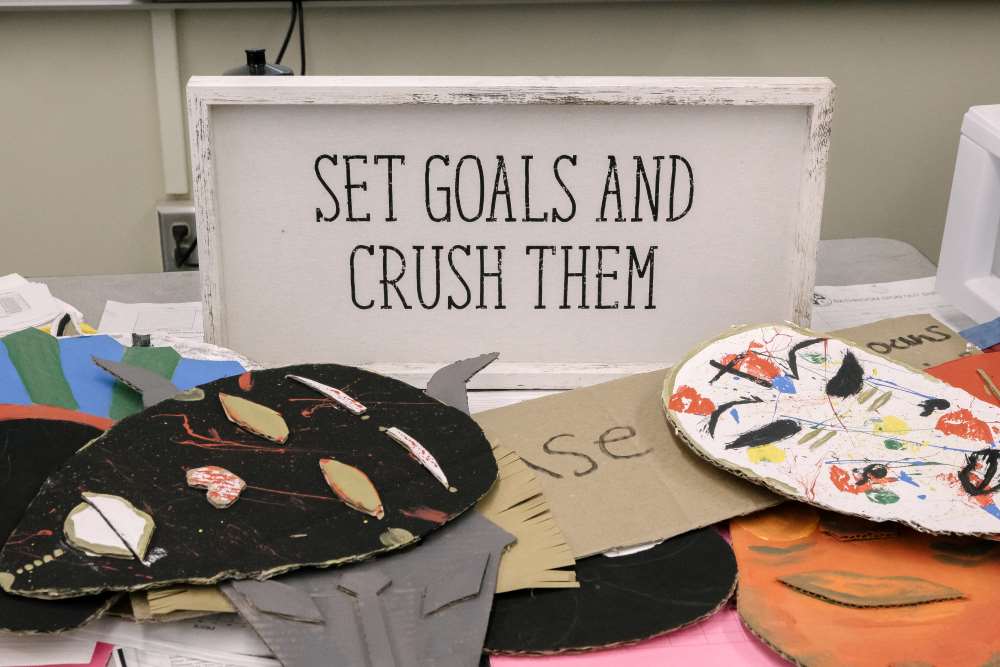 A table at NMSS is covered with colorful masks and a sign propped up that reads: Set goals and crush them.
